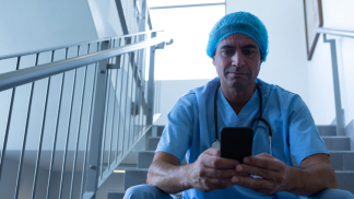 male-surgeon-using-mobile-phone-while-sitting-stairs-hospital-scaled.jpg